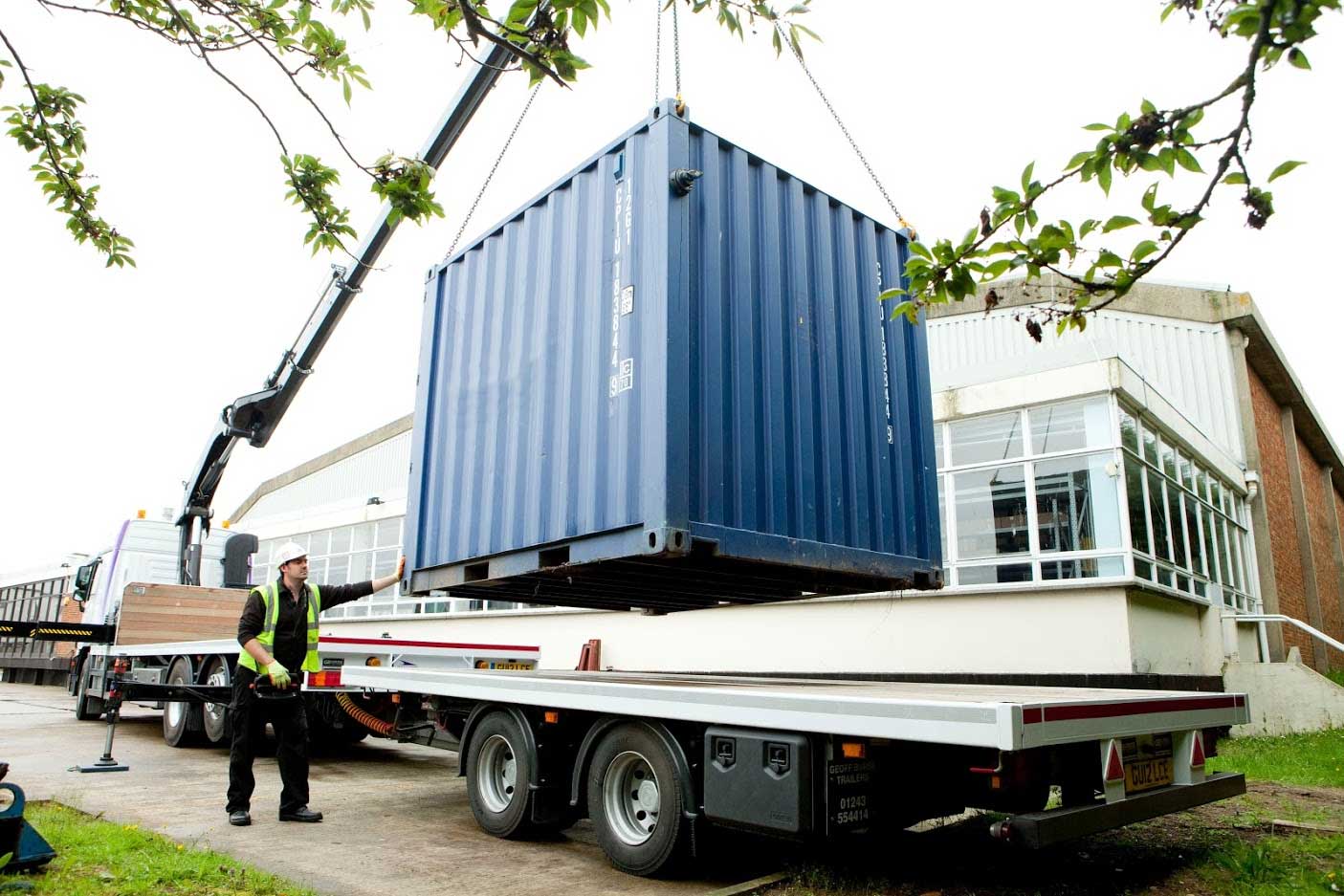 Blue square container being loaded onto flat bed truck.